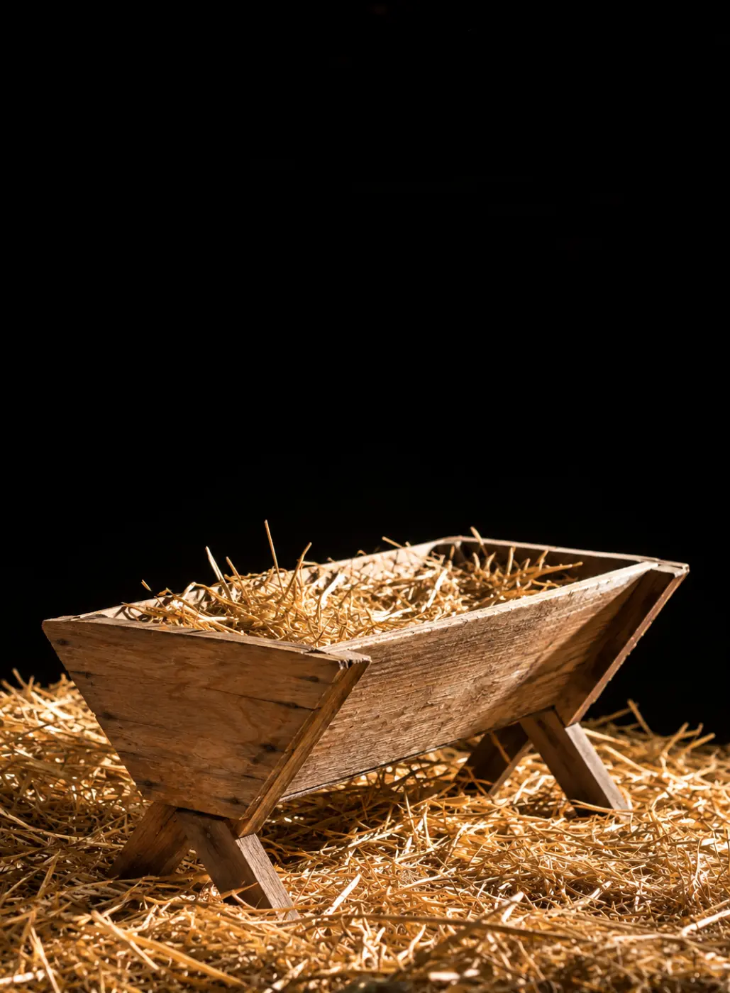 A wooden manger filled with straw sits on a bed of hay.